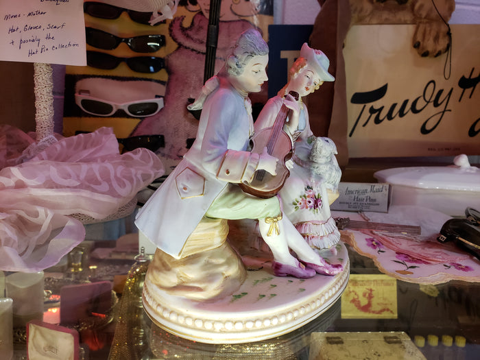 Man playing instrument to Lady holding Sheep figurine