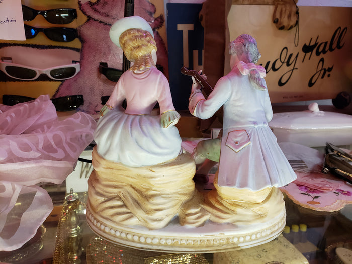 Man playing instrument to Lady holding Sheep figurine